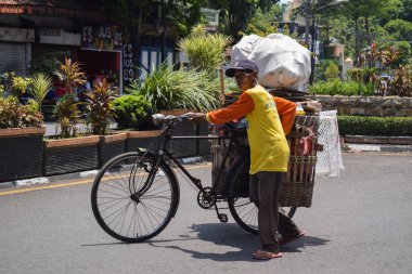 Pasuruan - October 31, 2022 : An old man carrying a bag, sack and paper case on his bicycle