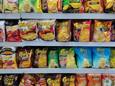 Pasuruan - November 12, 2022 : Various brands of local and imported potato chips and snacks on Supermarket Shelf.