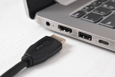 Adam siyah HDMI kablosunu beyaz arkaplandaki modern dizüstü bilgisayarın HDMI portuna bağlıyor