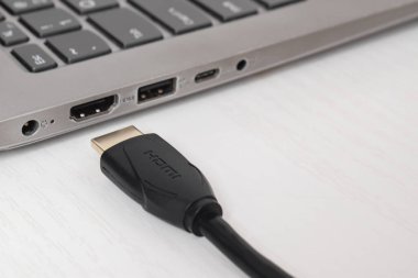 Adam siyah HDMI kablosunu beyaz arkaplandaki modern dizüstü bilgisayarın HDMI portuna bağlıyor