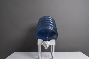 Gri arka planda izole edilmiş bir musluk ile ayakta duran bir rafta duran plastik bir galon.