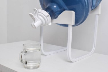 Beyaz arka planda izole edilmiş musluğu olan bir rafta duran plastik bir galon. Büyük su şişeli su dağıtıcısı.