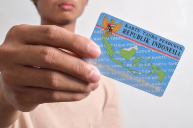 Beyaz arka planda bir kişi Endonezya kimlik kartlarını (KTP) gösterir ve tutar. Seçici odak