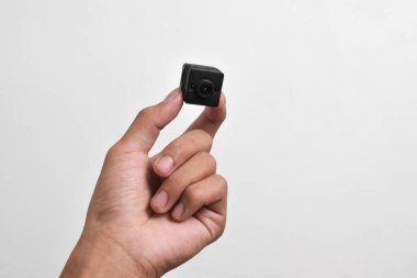 Elinde beyaz arka planda izole edilmiş bir casus kamerası var. Siyah güvenlik kamerası, Mini casus kamerası.