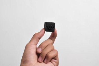 Elinde beyaz arka planda izole edilmiş bir casus kamerası var. Siyah güvenlik kamerası, Mini casus kamerası.