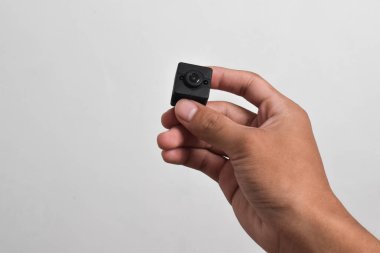 Elinde beyaz arka planda izole edilmiş bir casus kamerası var. Siyah güvenlik kamerası, Mini casus kamerası.