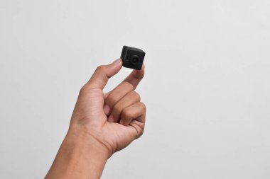 Elinde beyaz arka planda izole edilmiş bir casus kamerası var. Siyah güvenlik kamerası, Mini casus kamerası.