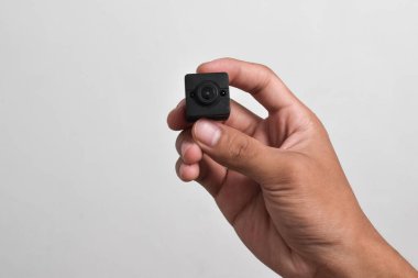 Elinde beyaz arka planda izole edilmiş bir casus kamerası var. Siyah güvenlik kamerası, Mini casus kamerası.