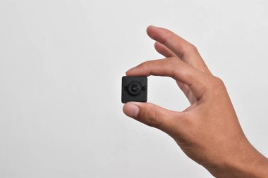 Elinde beyaz arka planda izole edilmiş bir casus kamerası var. Siyah güvenlik kamerası, Mini casus kamerası.