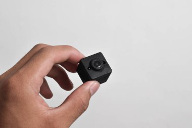 Elinde beyaz arka planda izole edilmiş bir casus kamerası var. Siyah güvenlik kamerası, Mini casus kamerası.