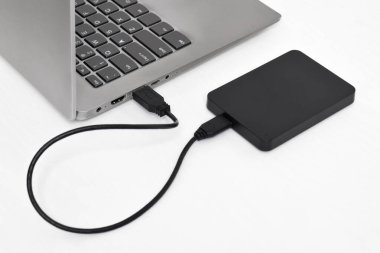 Beyaz arkaplandaki dizüstü bilgisayara bağlı harici yedek disk sürücüsü. USB 3.0 portu ile laptopa bağlanan harici sabit disk