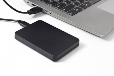 Beyaz arkaplandaki dizüstü bilgisayara bağlı harici yedek disk sürücüsü. USB 3.0 portu ile laptopa bağlanan harici sabit disk