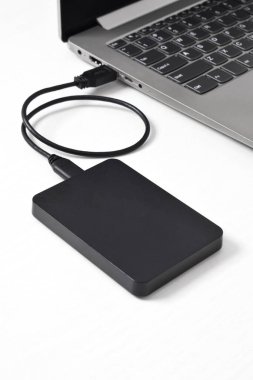 Beyaz arkaplandaki dizüstü bilgisayara bağlı harici yedek disk sürücüsü. USB 3.0 portu ile laptopa bağlanan harici sabit disk