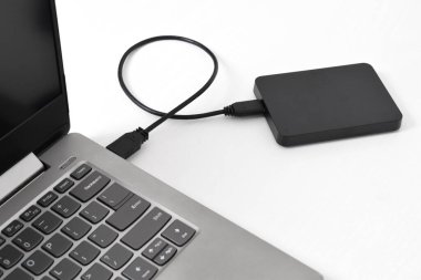 Beyaz arkaplandaki dizüstü bilgisayara bağlı harici yedek disk sürücüsü. USB 3.0 portu ile laptopa bağlanan harici sabit disk