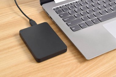 Tahta masadaki dizüstü bilgisayara bağlı harici yedek hard disk. USB 3.0 portu ile laptopa bağlanan harici sabit disk