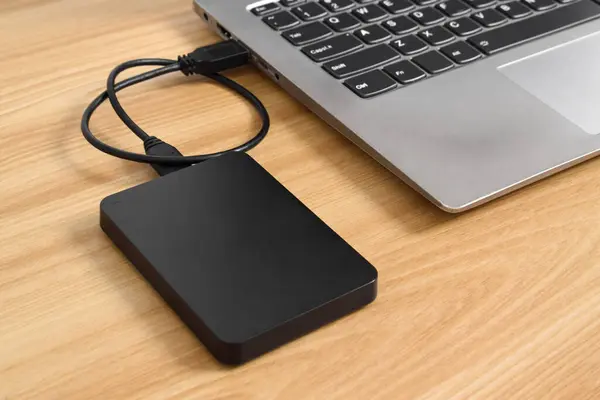 Tahta masadaki dizüstü bilgisayara bağlı harici yedek hard disk. USB 3.0 portu ile laptopa bağlanan harici sabit disk