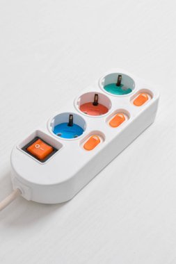 Beyaz arka planda izole edilmiş prizdeki beyaz elektrik prizi, güç kablosu, elektrik uzatma kablosu, üç soket, bir güç düğmesi ve bağlı bir elektrik prizi.