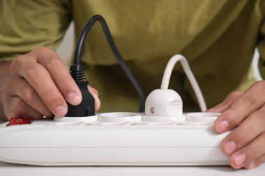 Bir adam enerji tüketimini azaltmak için beyaz bir elektrik prizinin elektrik akımını kesiyor.