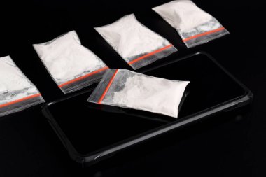 Siyah arka planda izole edilmiş akıllı telefondaki plastik pakette kokain. Yasadışı uyuşturucu maddelerinin ve uyuşturucuların gösterimi