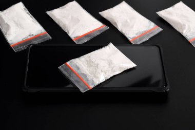 Siyah arka planda izole edilmiş akıllı telefondaki plastik pakette kokain. Yasadışı uyuşturucu maddelerinin ve uyuşturucuların gösterimi