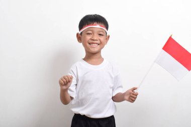 17 Ağustos 'ta beyaz arka planda izole edilmiş, Endonezya Bağımsızlık Günü' nü kutlamak için bayrak takan mutlu yüzlü, tatlı Asyalı çocuk..