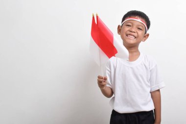 Endonezya 'nın Bağımsızlık Günü' nü kutlamak için 17 Ağustos 'ta beyaz arka planda izole edilmiş Endonezya bayrağını tutan sevimli küçük Asyalı çocuk..