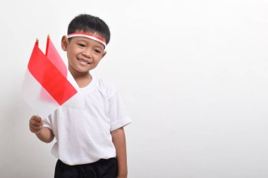 Endonezya 'nın Bağımsızlık Günü' nü kutlamak için 17 Ağustos 'ta beyaz arka planda izole edilmiş Endonezya bayrağını tutan sevimli küçük Asyalı çocuk..