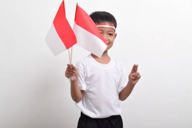 Endonezya bayrağını tutan sevimli küçük Asyalı çocuk, 17 Ağustos 'taki Bağımsızlık Günü' nü kutlamak için beyaz arka planda barışçıl bir jest yaparak iki parmağını gösteriyor..