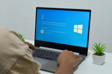 Pasuruan, Endonezya - 20 Temmuz 2024: Dizüstü bilgisayarlı bir adam mavi ölüm ekranını veya BSOD 'u monitörde gösterir. Hatalı Microsoft Windows işletim sistemi. Mavi ölüm perdesi