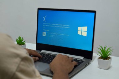 Pasuruan, Endonezya - 20 Temmuz 2024: Dizüstü bilgisayarlı bir adam mavi ölüm ekranını veya BSOD 'u monitörde gösterir. Hatalı Microsoft Windows işletim sistemi. Mavi ölüm perdesi