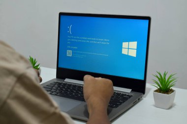 Pasuruan, Endonezya - 20 Temmuz 2024: Dizüstü bilgisayarlı bir adam mavi ölüm ekranını veya BSOD 'u monitörde gösterir. Hatalı Microsoft Windows işletim sistemi. Mavi ölüm perdesi