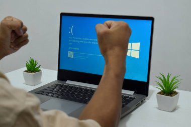 Pasuruan, Endonezya - 20 Temmuz 2024: Dizüstü bilgisayarlı bir adam mavi ölüm ekranını veya BSOD 'u monitörde gösterir. Hatalı Microsoft Windows işletim sistemi. Mavi ölüm perdesi