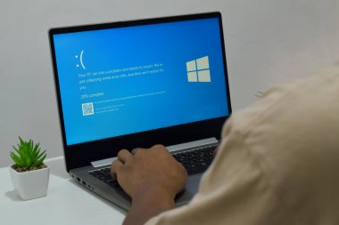 Pasuruan, Endonezya - 20 Temmuz 2024: Dizüstü bilgisayarlı bir adam mavi ölüm ekranını veya BSOD 'u monitörde gösterir. Hatalı Microsoft Windows işletim sistemi. Mavi ölüm perdesi