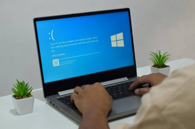 Pasuruan, Endonezya - 20 Temmuz 2024: Dizüstü bilgisayarlı bir adam mavi ölüm ekranını veya BSOD 'u monitörde gösterir. Hatalı Microsoft Windows işletim sistemi. Mavi ölüm perdesi