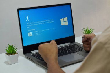 Pasuruan, Endonezya - 20 Temmuz 2024: Dizüstü bilgisayarlı bir adam mavi ölüm ekranını veya BSOD 'u monitörde gösterir. Hatalı Microsoft Windows işletim sistemi. Mavi ölüm perdesi