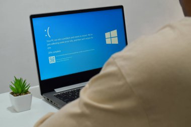 Pasuruan, Endonezya - 20 Temmuz 2024: Dizüstü bilgisayarlı bir adam mavi ölüm ekranını veya BSOD 'u monitörde gösterir. Hatalı Microsoft Windows işletim sistemi. Mavi ölüm perdesi