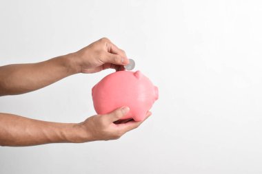 El, beyaz arka planda izole edilmiş kumbaraya bozuk para koyuyor. Emeklilik fonu ve gelecek planlama konsepti için para biriktirme.