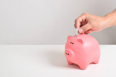 El, beyaz arka planda izole edilmiş kumbaraya bozuk para koyuyor. Tasarruf, yatırım ve finans kavramı. Mesaj için yer var. Boşluğu kopyala