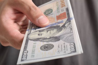 Adam elini dolar banknotuna uzatıyor. El ele tutuşan dolar, 100 dolar banknot.