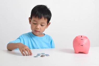 Asyalı küçük çocuk, beyaz arka planda izole edilmiş pembe kumbaralarda para biriktiriyor. Çocuk konsepti için para biriktiriyorum. Tasarruf etmeyi öğren. Para, finans ve sigorta kavramı