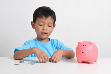 Asyalı küçük çocuk, beyaz arka planda izole edilmiş pembe kumbaralarda para biriktiriyor. Çocuk konsepti için para biriktiriyorum. Tasarruf etmeyi öğren. Para, finans ve sigorta kavramı