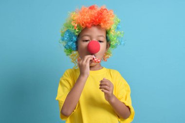 Mavi arka planda soytarı peruğu, palyaço burnu ve parti düdüğü olan şirin Asyalı çocuk. Boşluğu kopyala