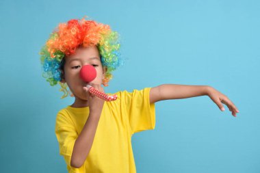 Mavi arka planda soytarı peruğu, palyaço burnu ve parti düdüğü olan şirin Asyalı çocuk. Boşluğu kopyala