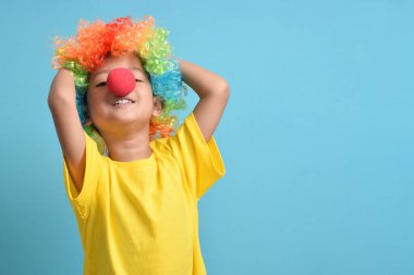Mavi arka planda palyaço peruğu ve palyaço burnu olan sevimli Asyalı çocuk. Boşluğu kopyala