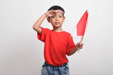 Kırmızı tişörtlü mutlu Asyalı çocuk beyaz arka planda izole edilmiş bayrak takıyor. Endonezya Bağımsızlık Günü konsepti