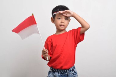 Kırmızı tişörtlü mutlu Asyalı çocuk beyaz arka planda izole edilmiş bayrak takıyor. Endonezya Bağımsızlık Günü konsepti