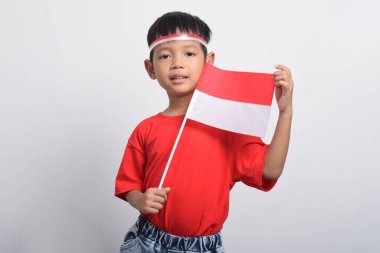 Mutlu bir Asyalı çocuk Endonezya bayrağını tutuyor ve kendinden emin bir tavırla gülümsüyor, beyaz arka planda soyutlanmış. Endonezya Bağımsızlık Günü konsepti.
