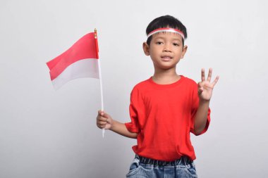 Kırmızı tişörtlü mutlu bir Asyalı çocuk beyaz arka planda iyi ve güzel hareketler yapıyor. Endonezya Bağımsızlık Günü konsepti.