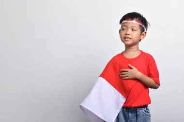 Endonezya bayrağı omzunda, beyaz arka planda soyutlanmış bir şekilde mutlu bir şekilde gülümseyen Asyalı çocuk. Endonezya Bağımsızlık Günü konsepti.