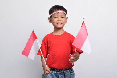 Kırmızı tişörtlü mutlu bir Endonezyalı, elinde iki bayrak beyaz arka planda izole edilmiş bir şekilde gülümsüyor. Endonezya Bağımsızlık Günü konsepti.